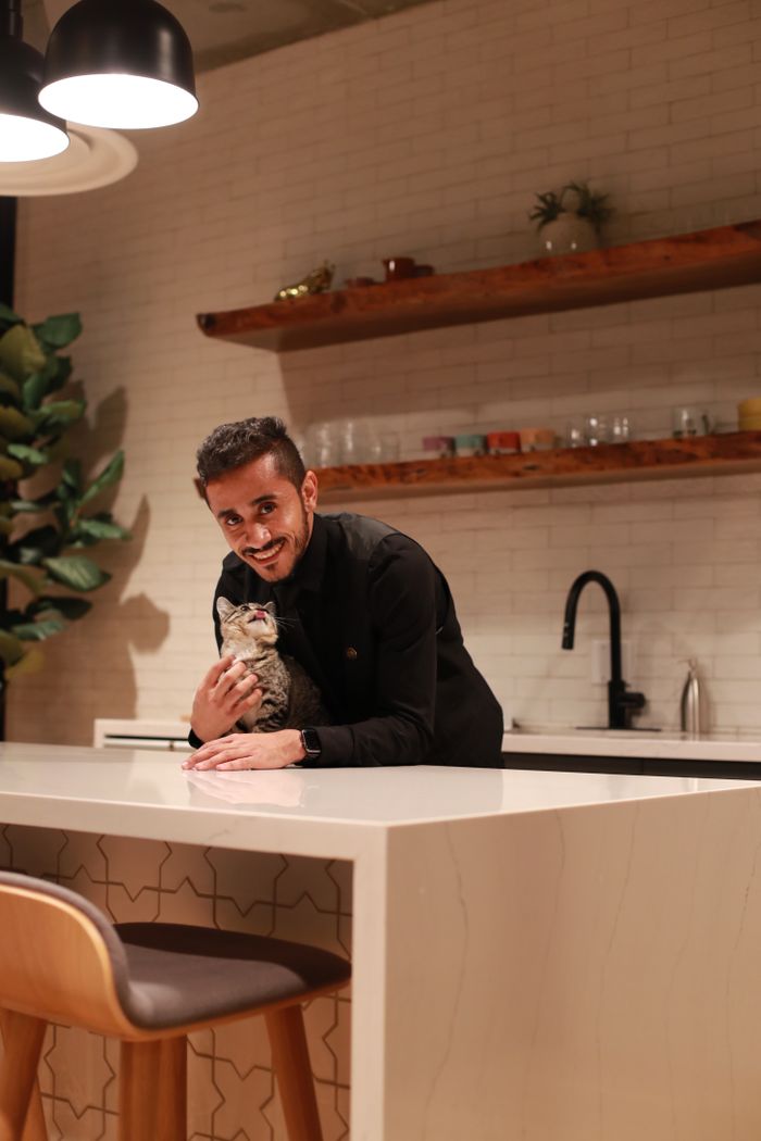 gallery-6 A man smiling while holding a cat in a stylish kitchen with underlit counters.